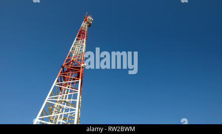 Looking up to small red and white telecommunications tower, communication dishes on top. Abstract technology background, space for text on right. Stock Photo