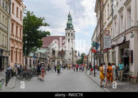 People walking along cobblestone street with Saints Peter and Paul Church rising above them in Main Market Square of Krak—w Old Town, Lesser Poland Vo Stock Photo