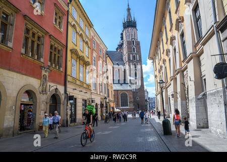 People walking and enjoying themselves along the cobblestone streets of Main Market Square in Krak—w Old Town with Church of Our Lady Assumed into Hea Stock Photo