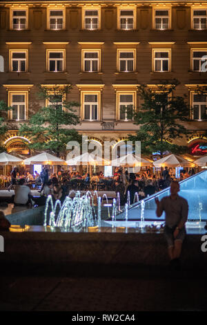 People walking, eating and enjoying the Main Market Square of Krak—w Old Town at night with fountain in front, Lesser Poland Voivodeship, Poland. Stock Photo