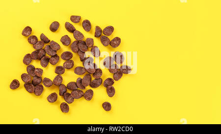 Top down view, scattered chocolate cornflake on yellow board, space for text on the right. Stock Photo