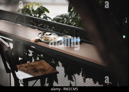 Abstract scene of breakfast meal set including tuna sandwich, hot long black coffee, and brownie cheese cake on outdoor wood bar. Weekend morning acti Stock Photo