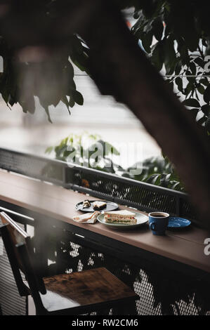 Abstract scene of breakfast meal set including tuna sandwich, hot long black coffee, and brownie cheese cake on outdoor wood bar. Weekend morning acti Stock Photo