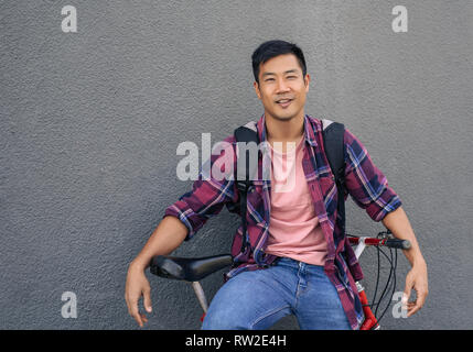 Smiling young man leaning with his bike against a wall Stock Photo