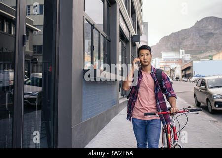 Young man walking with his bike talking on a cellphone Stock Photo