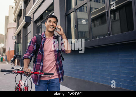 Smiling man walking with his bike talking on a cellphone Stock Photo