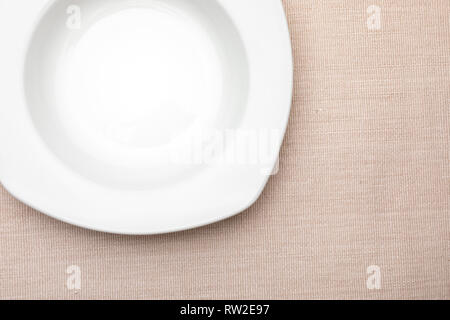 Empty white plate. On delicate beige tablecloth. Concept to include your food and your text. Stock Photo
