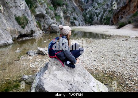 Child alone hiking sitting near a mountain lake resting on the trail Stock Photo