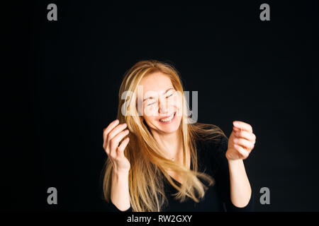 Close up studio portrait of a beautiful woman in the black dress, laughing, eyes closed, against the black background Stock Photo