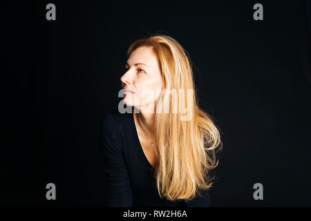 Close up studio portrait of a beautiful woman in the black dress against black background Stock Photo