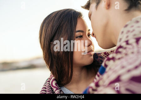 Young couple wrapped in a blanket about to kiss outside Stock Photo
