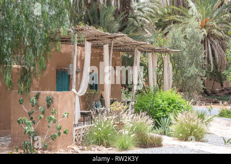 Exterior of traditional mud-brick constructed house with thatched roof covering front porch area, Tighmert Oasis, Morocco Stock Photo