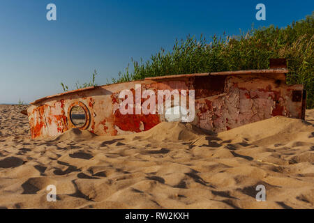 Abandoned, old, dilapidated boat carcass on a Baltic sea beach on a green reed background. Stock Photo