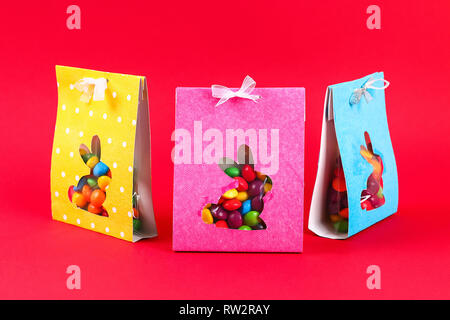 Diy Easter wrapping package sweets in a bag with a cut out bunny silhouette on a red background. Gift idea, decor Spring, Easter. Step by step. Top vi Stock Photo