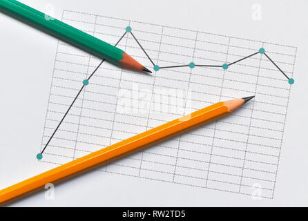 Broken line chart representing the data and two pencils on bright background Stock Photo