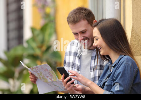 Happy couple of tourists checking smart phone and map searhing location in the street on vacation Stock Photo