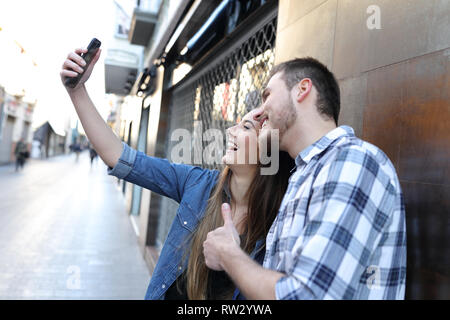 Happy couple taking selfies with smart phone standing in the street Stock Photo