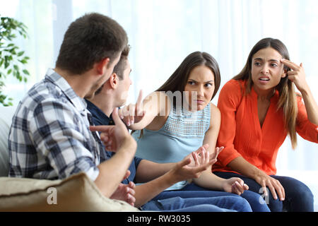 Two angry men and women arguing sitting on a couch in the living room at home Stock Photo