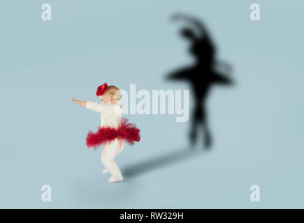 Baby girl dreaming about dancing ballet. Childhood and dream concept. Conceptual image with shadow of ballerina on the studio wall Stock Photo
