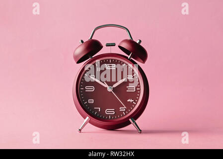 Old fashioned red alarm clock with bells centered over a pink background with lateral copy space Stock Photo