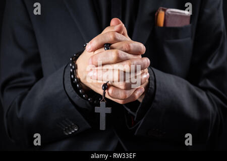 Christian person praying, low key image. Hands of a man in black suit or a priest portraying a preach Stock Photo