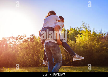Happy young couple in love having fun in spring forest. Man rides his girlfriend on back at sunset. Guys chilling outside Stock Photo