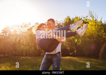 Happy couple in love having fun in spring forest. Man holds his girlfriend in hands and spins at sunset. Stock Photo