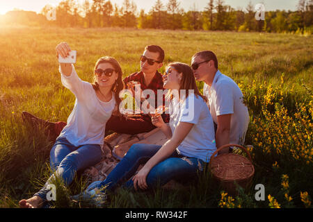 Friends eating pizza outside and having fun. Women and men having picnic at sunset. Young people hanging together. Fast food concept. Stock Photo