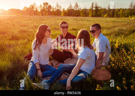 Friends hanging out and eating pizza outside. Women and men having picnic at sunset. Guys spending good time together and having fun. Stock Photo