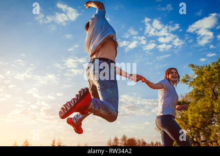 Young man and woman running and jumping. Happy couple having fun in spring field at sunset. Stock Photo