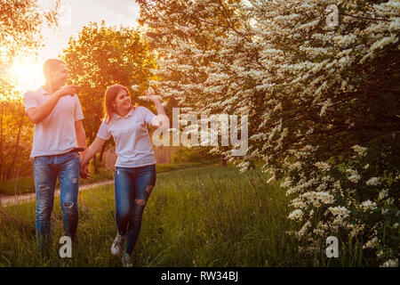 Couple walking in spring blossoming park at sunset. Young man and woman having good time together Stock Photo