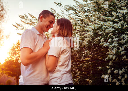 Happy couple walking in spring blooming park at sunset. Young man and woman holding hands and smiling Stock Photo