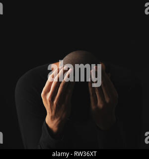 closeup of a desperate young caucasian man with his hands in his head, against a black background Stock Photo