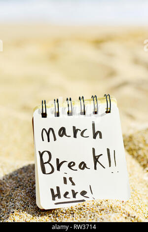 closeup of a notepad with the text march break is here written in it, on the sand of a quiet beach, with some blank space on top Stock Photo