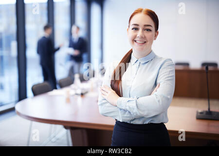 Waist up portrait of pretty young businesswoman smiling at camera while posing in conference room, copy space Stock Photo