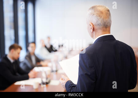Back view portrait of senior businessman giving speech in conference room talking to employees, copy space Stock Photo
