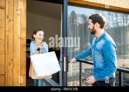 Young couple entering home carrying shopping bags. Happy purchase and modern living concept