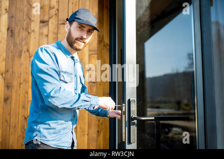 Workman repairing entrance door lock of the modern house or hotel during the sunny weather outdoors Stock Photo
