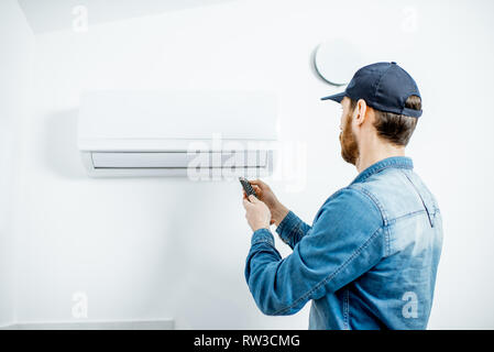 Repairman in blue workwear serving the air conditioner controling with remote on the white wall background Stock Photo