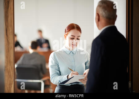 Waist up portrait of young woman holding clipboard talking to boss or business coach, copy space Stock Photo