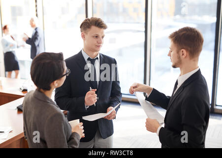 Group of young entrepreneurs communicating after business meeting in office, copy space Stock Photo