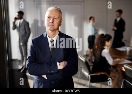 Waist up portrait of pensive senior man standing with arms crossed in conference room, copy space Stock Photo