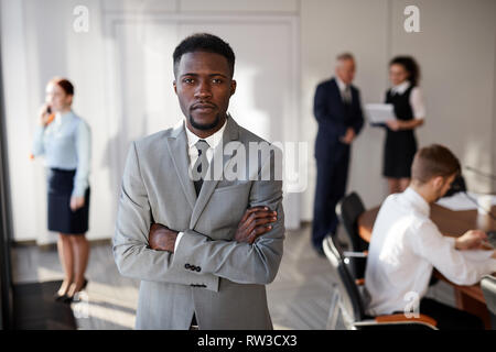 Waist up portrait of African-American businessman standing with arms crossed in conference room, copy space Stock Photo