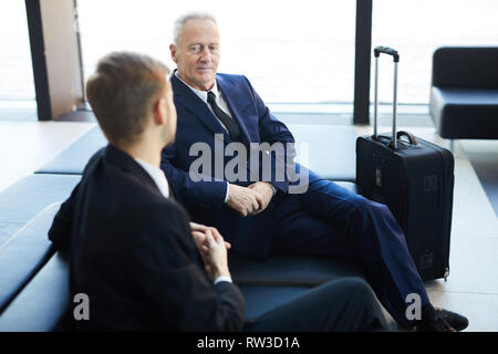 High angle portrait of senior businessman talking to partner while waiting in airport lobby, copy space Stock Photo