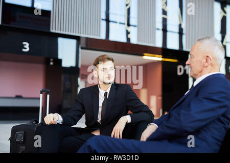 Portrait of successful young businessman talking to partner while waiting in airport lobby, copy space Stock Photo