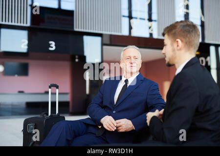 Portrait of successful senior businessman talking to partner while waiting in airport lobby, copy space Stock Photo