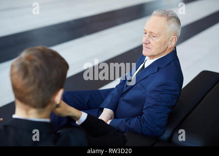 Graphic portrait of successful senior businessman sitting on sofa in office or lobby, copy space Stock Photo