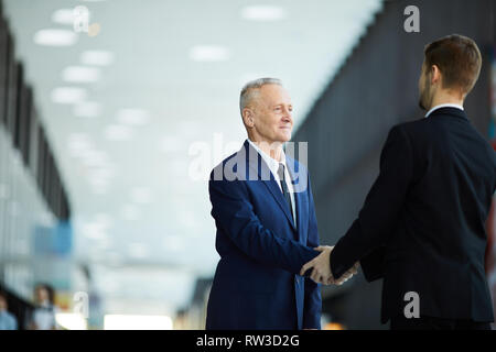 Waist up portrait of successful senior businessman shaking hands with partner standing in hall of business center, copy space Stock Photo