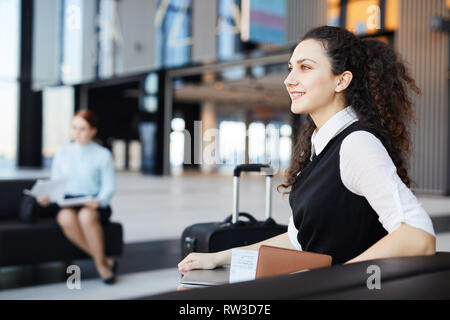 Side view portrait of smiling young woman waiting in airport lobby excited for travelling, copy space Stock Photo