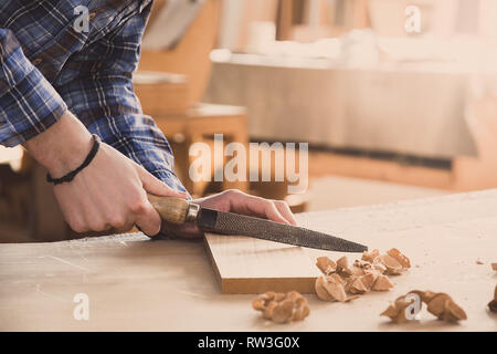Carpenter working with rasp on wood using rasper. Workshop background. Carpenter workbench. Stock Photo